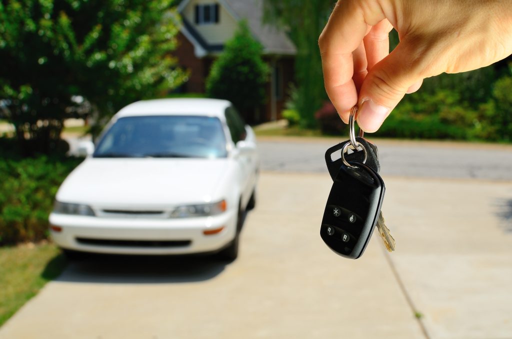 Car keys in hand with white car background.